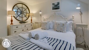 Un dormitorio con cama, espejo redondo, mesita de noche, lámpara, luz empotrada en la pared y un cuadro enmarcado.
