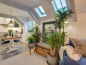 Een ruime loft met keuken, eethoek en woonkamer. Er zijn dakramen, potplanten en een gezellige zithoek.