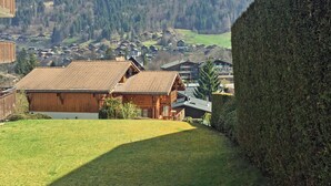 A wooden cabin with a sloped roof, surrounded by a well-maintained lawn and a tall hedge. - Modern, luxury studio in Morzine,1st floor, sleeps 4, centrally located (Morzine)