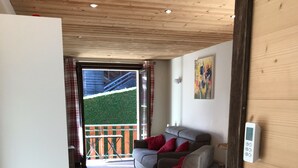 A cozy living area with a sofa, a small table, and a view of a balcony with a wooden railing. - Modern, luxury studio in Morzine,1st floor, sleeps 4, centrally located (Morzine)