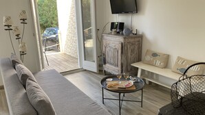 Moderni olohuone, jossa on sohva, pyöreä sohvapöytä, jolla on tarjolla pientä purtavaa, seinälle asennettu televisio ja liukuovi, joka johtaa ulkotilaan.