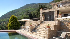 Een stenen villa met een zwembad, buitenmeubilair en een berg op de achtergrond.