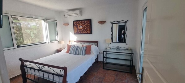 A bedroom with a bed, a bedside table, a mirror, and a window.