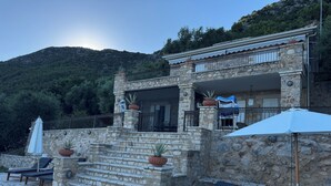 A stone building with a pool, outdoor seating, and a view of a mountainous area.
