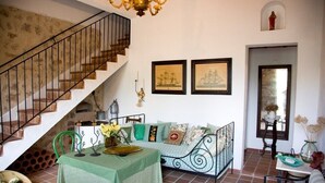 A cozy living room with a staircase, a sofa, a dining table with a green tablecloth, and two framed pictures on the wall.