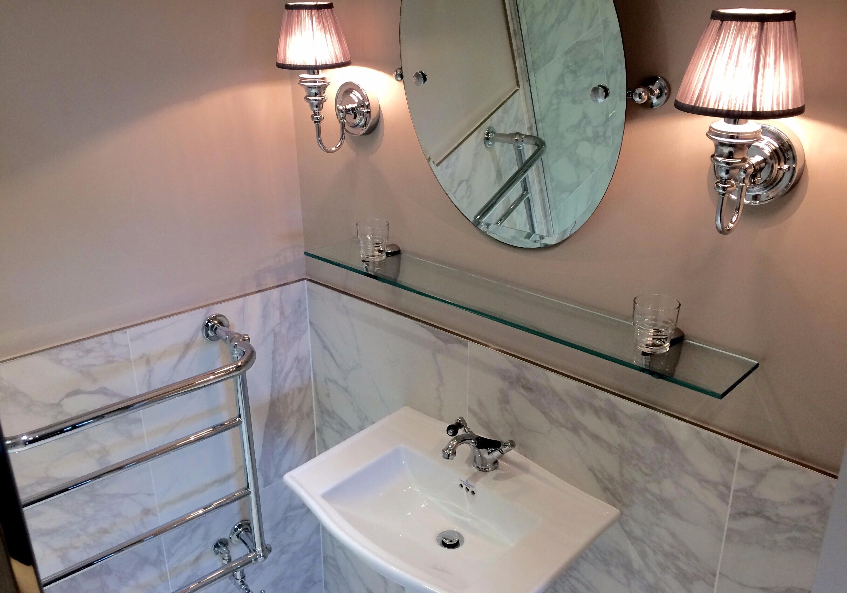 A bathroom with a white sink, two wall-mounted lamps, a glass shelf, and a towel rack.