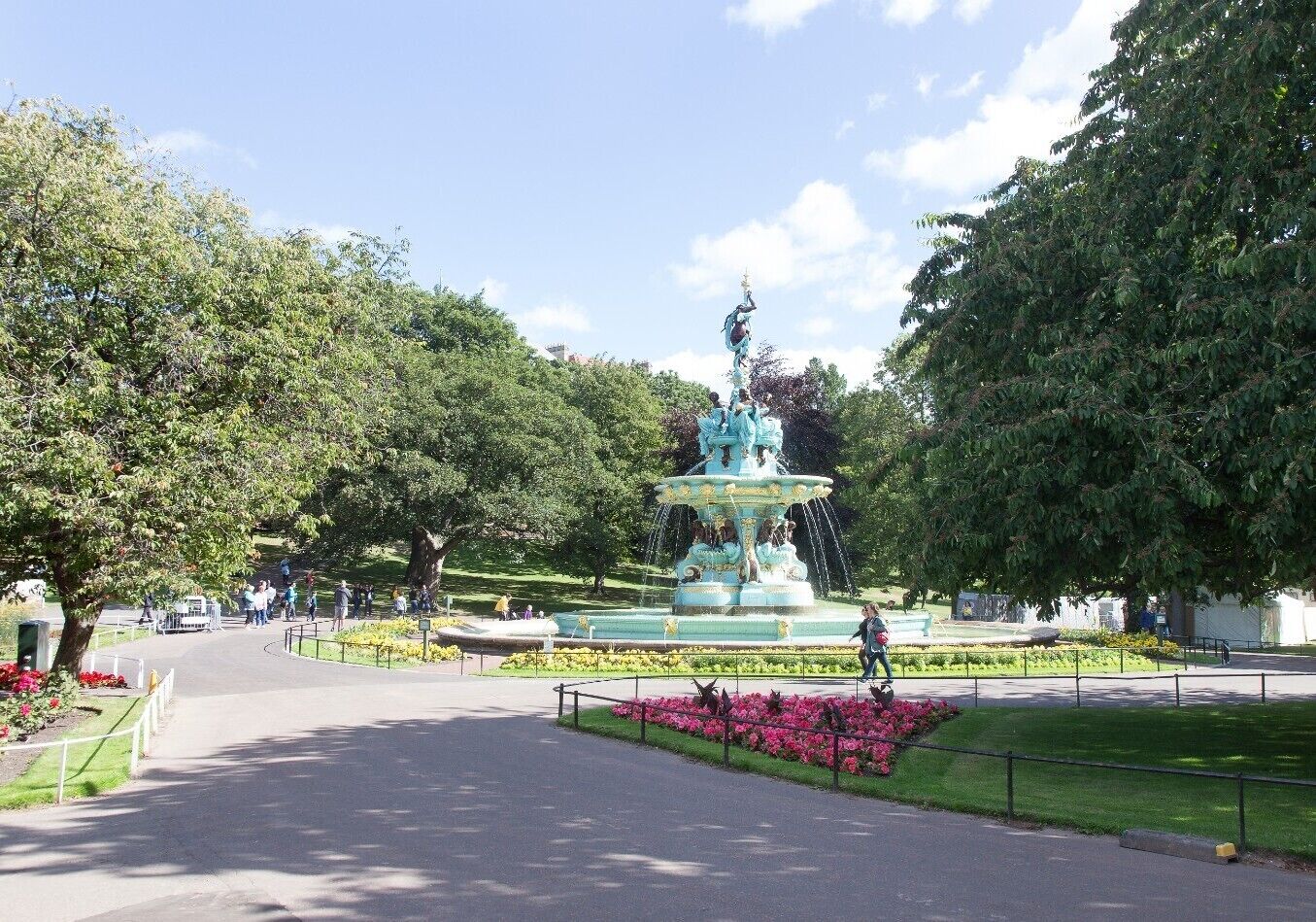 Un parque con una fuente central, rodeado de árboles y parterres florales.