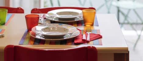 Mesa lista con platos, vasos y cubiertos, con vistas a un jardín verde y un coche rojo a través de un ventanal.