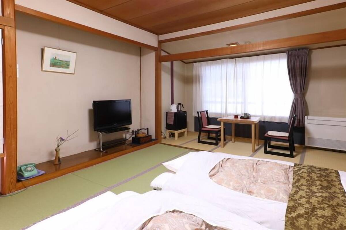 A hotel room with a bed, a television, a desk with a chair, and a window with curtains.