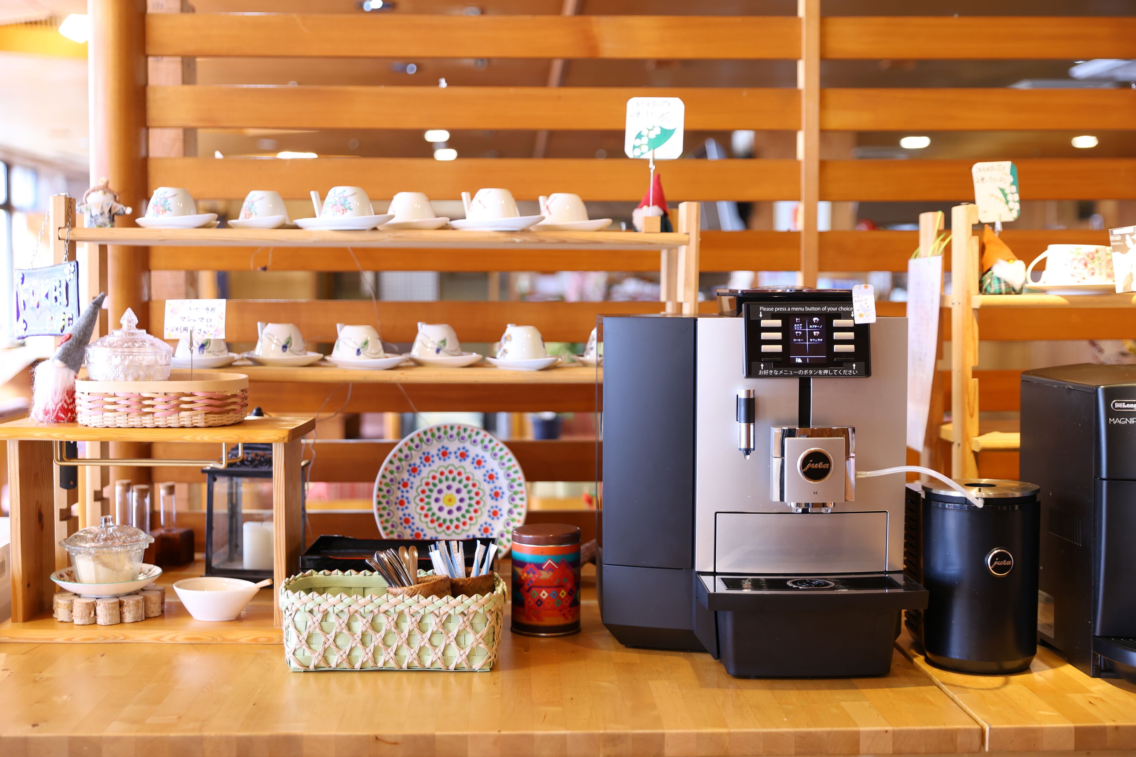 Interior de una cafetería con una máquina de café, estantes llenos de tazas y una barra de madera.