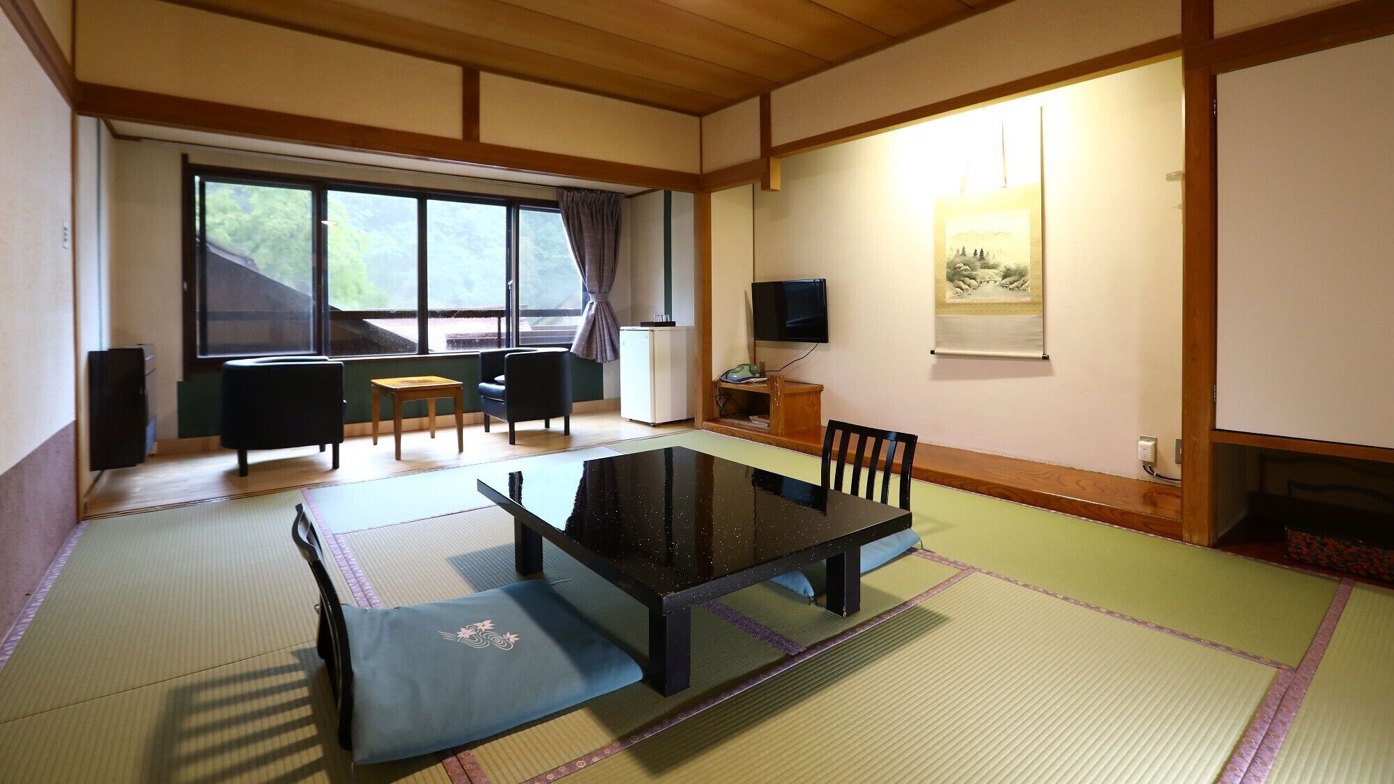 Una habitació japonesa tradicional amb tatami, una taula baixa, cadires, una televisió i una finestra amb vistes.