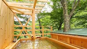 A wooden hot spring bath with a wooden roof and walls, surrounded by lush green trees. - Fukeikan (Takayama)