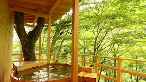 A wooden hot spring bath area with a wooden bench, surrounded by a wooden railing, set in a forested area. - Fukeikan (Takayama)