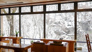 A wooden deck with seating and potted plants, large windows with a view of snow-covered trees. - Fukeikan (Takayama)