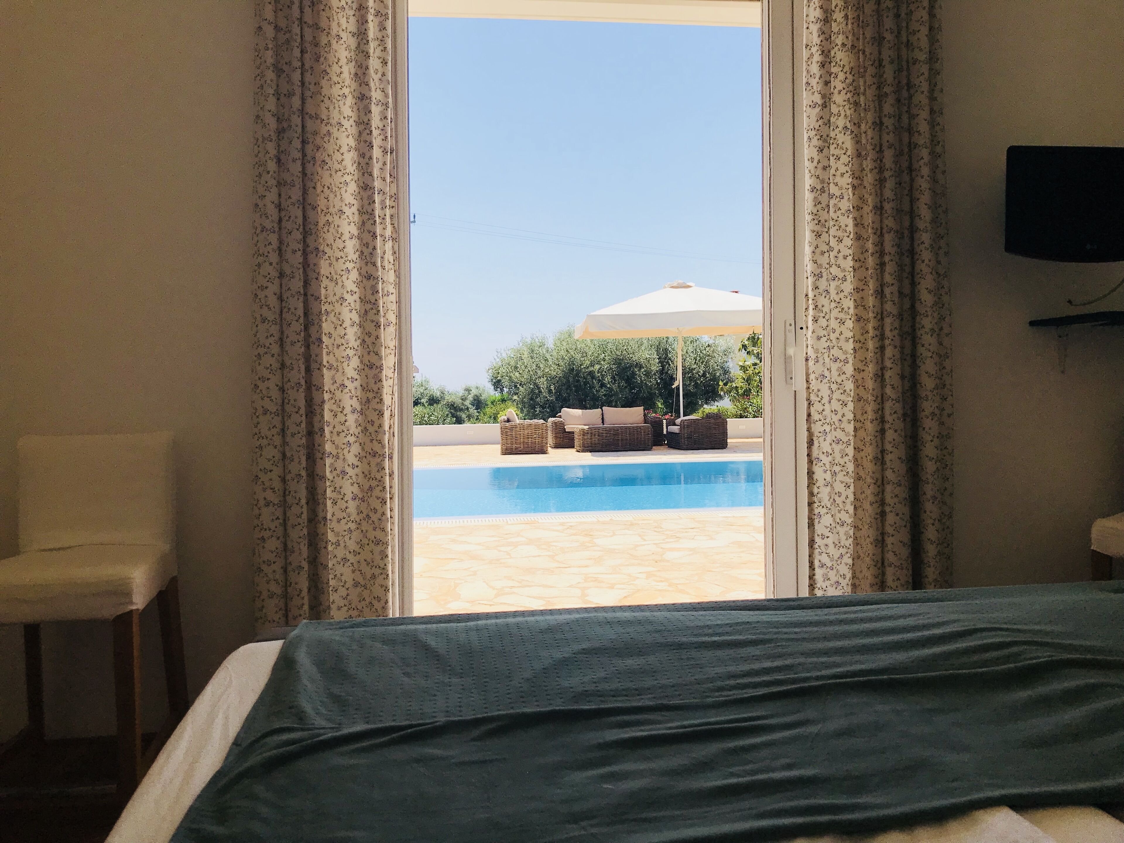 A hotel room with a bed, a chair, and a view of an outdoor swimming pool with lounge chairs.