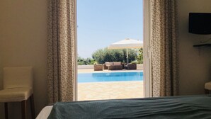 Habitació d'hotel amb llit, una cadira i vista a una piscina exterior amb gandules.