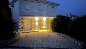 Una casa de dos pisos amb façana de pedra, un balcó i un vestíbul pavimentat amb pedra.