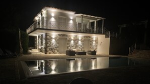 Una casa de dues plantes amb piscina davant, parets de pedra i mobiliari per a l'exterior.