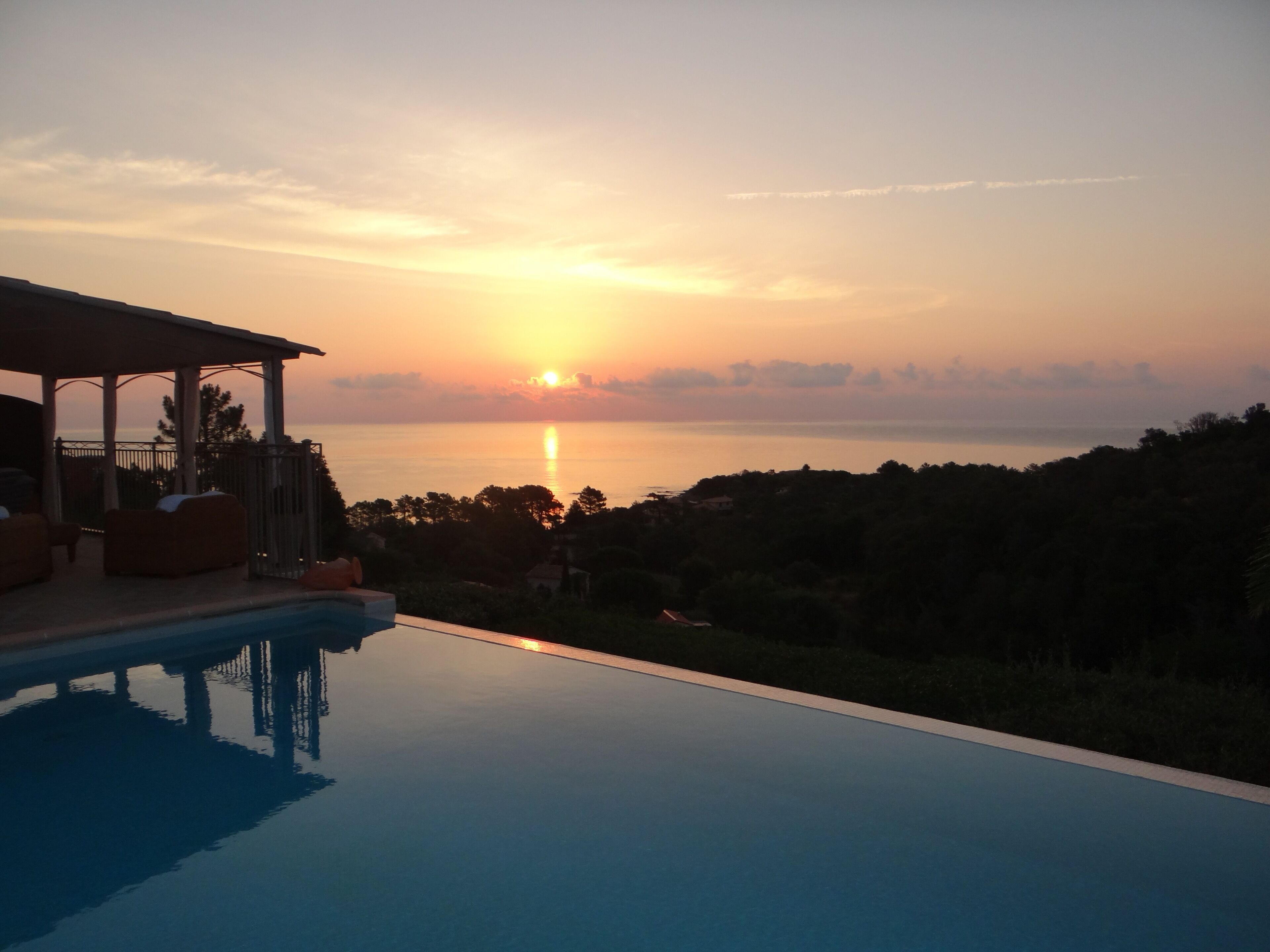 A swimming pool with a sunset view, lounge chairs, and a covered patio area.