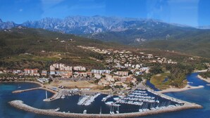 An aerial view of a coastal town with a marina, residential buildings, and mountains in the background. - house / villa - Solenzara (Sari-Solenzara)
