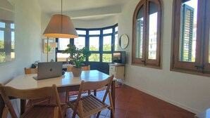 A dining area with a table, chairs, a laptop, a plant, and a television.