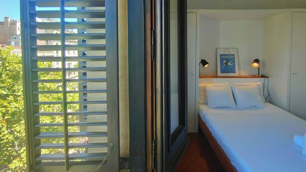 A hotel room with a bed, two bedside lamps, a framed picture on the wall, and a window with blinds.