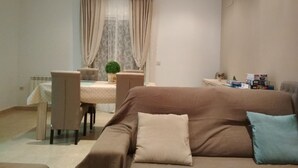 A modern living room with a brown sofa, a dining table with chairs, and a small potted plant.