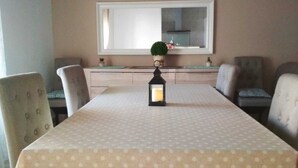 A dining table with a polka dot tablecloth, surrounded by four chairs, a small lantern, and a window with a view of the outside.