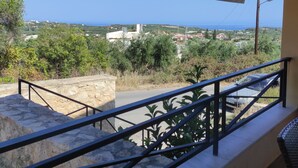 Un balcon doté d’un mur en pierre et d’une balustrade en métal, offrant une vue sur une ville côtière avec ses bâtiments et sa végétation.
