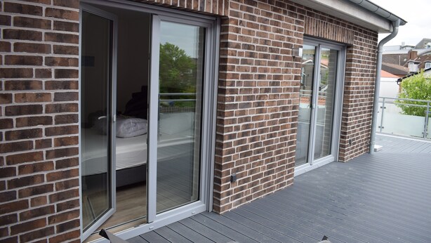A modern building with a brick exterior and large sliding glass doors leading to a balcony. - Apart Seegras Exclusive vacation apartment in a prime location! (Büsum)