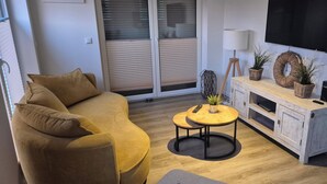A modern living room with a sofa, a round wooden coffee table, a TV, and a wooden cabinet with plants. - Apart Seegras Exclusive vacation apartment in a prime location! (Büsum)