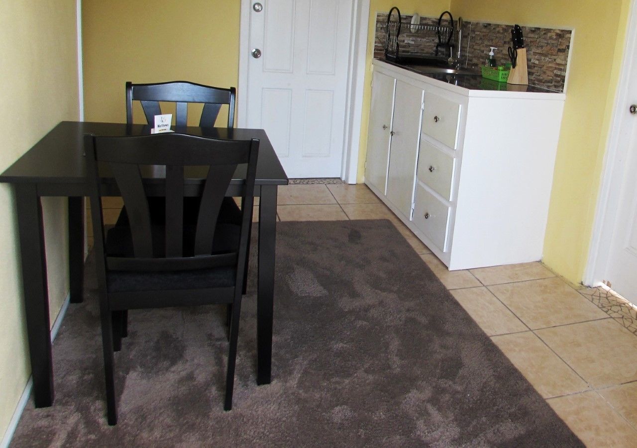 Una cocina pequeña con una mesa de comedor y sillas, una puerta blanca y una encimera con utensilios de cocina.