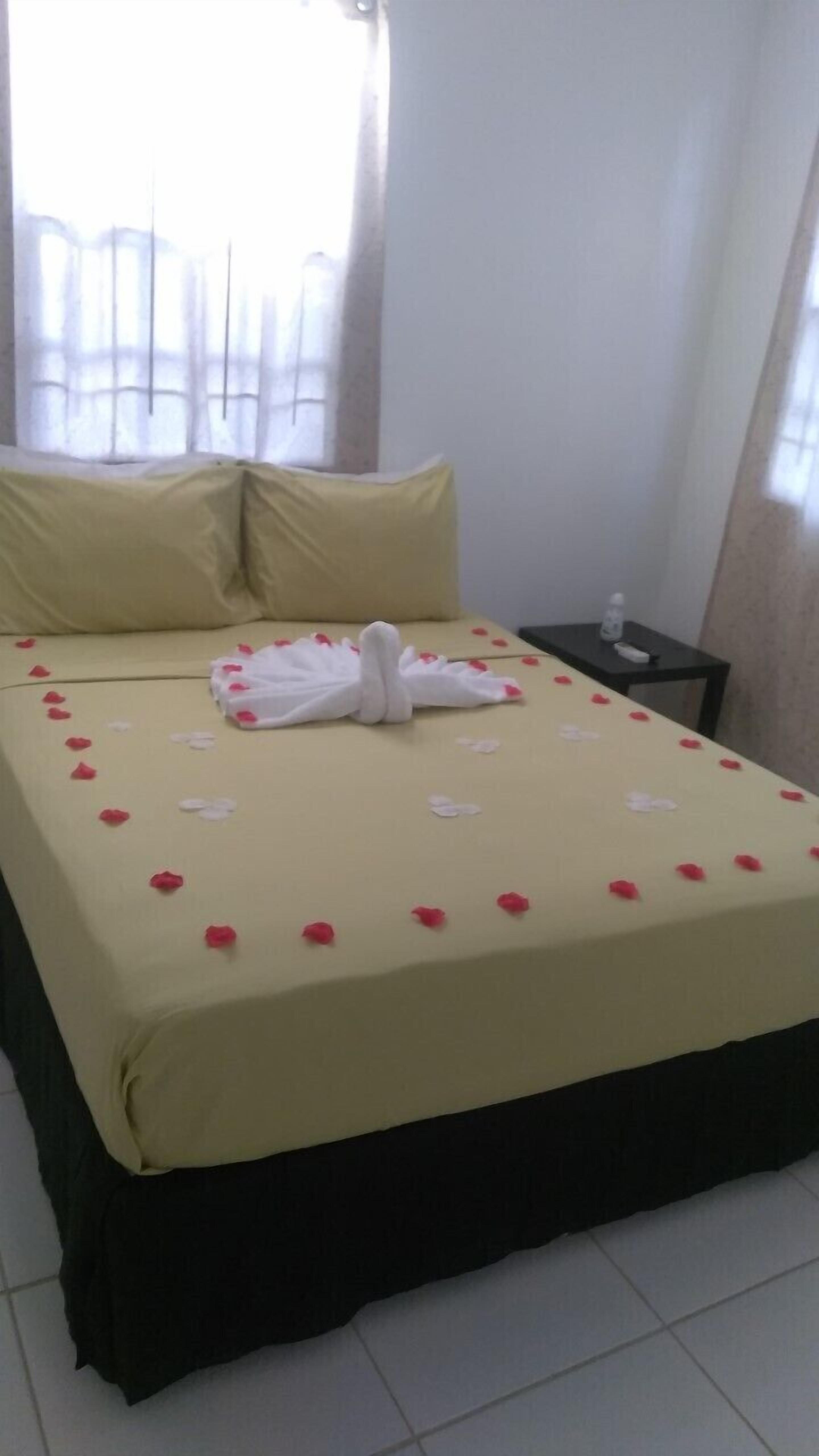 Ein ordentlich gemachtes Bett mit einer gelben Tagesdecke, weißen Kissen und einem in Schwanform drapierten Handtuch.