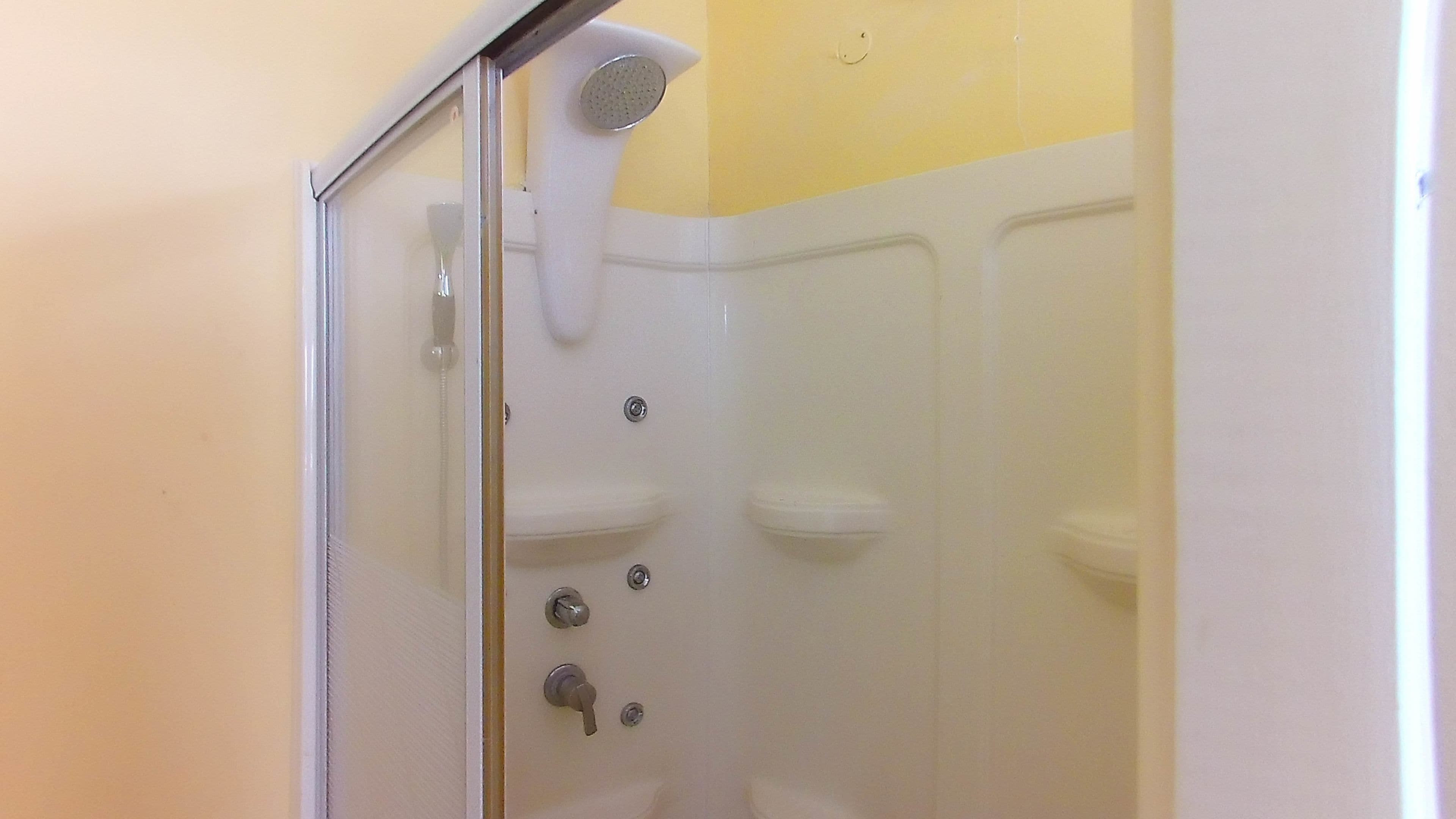 Ducha con cabezal de ducha de mano, puerta de vidrio y pared blanca con detalle amarillo.