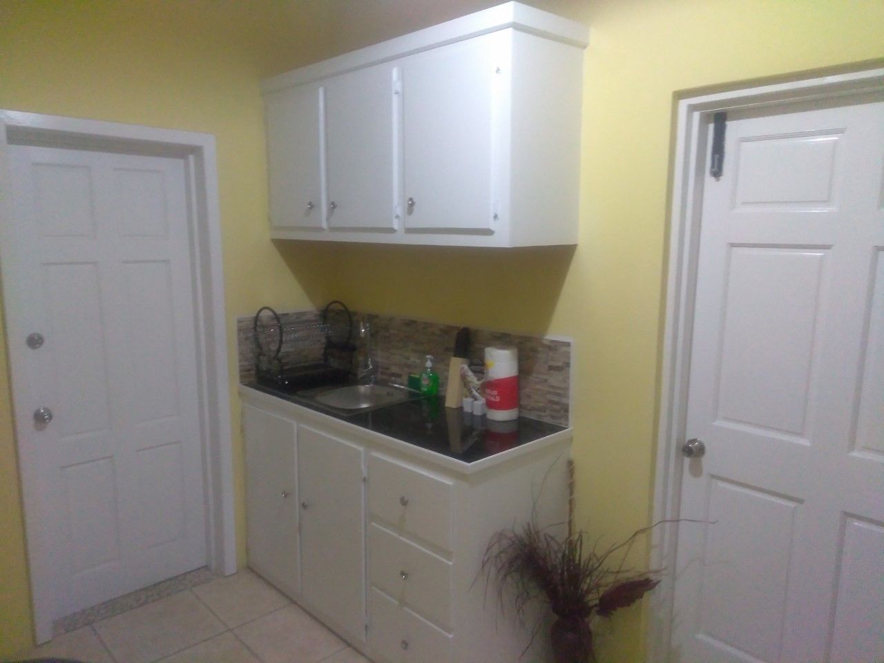 Una cocina pequeña con armarios blancos, encimera negra y un lavabo.