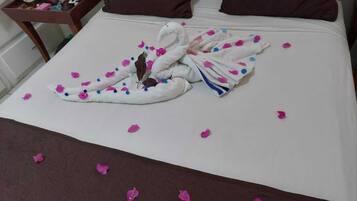Een bed met een handdoek gevouwen in de vorm van een zwaan, rozenblaadjes verspreid over het bed en een gestreept kussen.
