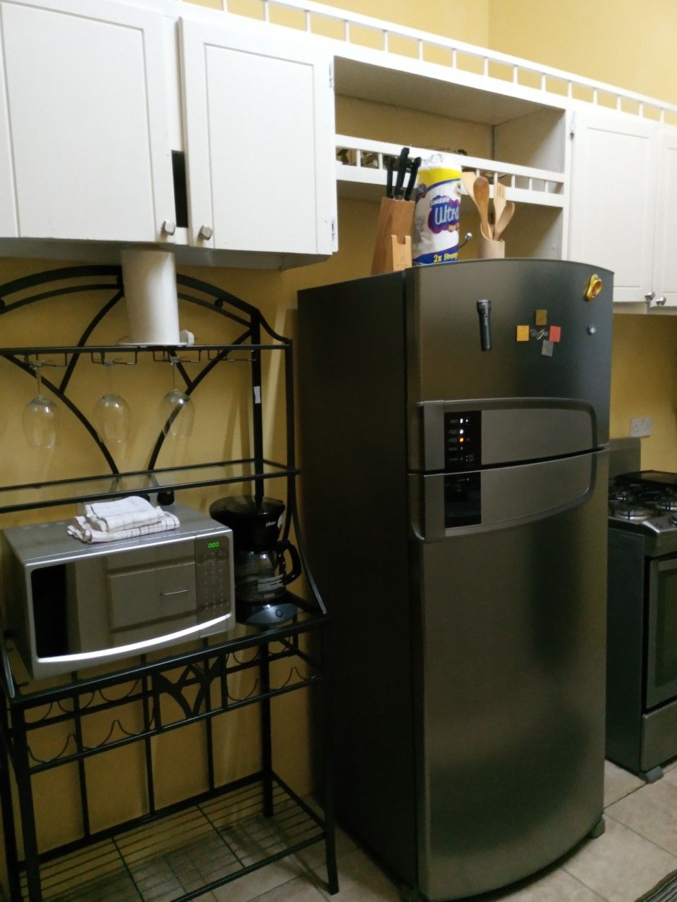 Eine Küche mit einem Edelstahl-Kühlschrank, einer Mikrowelle und einer Kaffeemaschine auf einer schwarzen Arbeitsplatte.