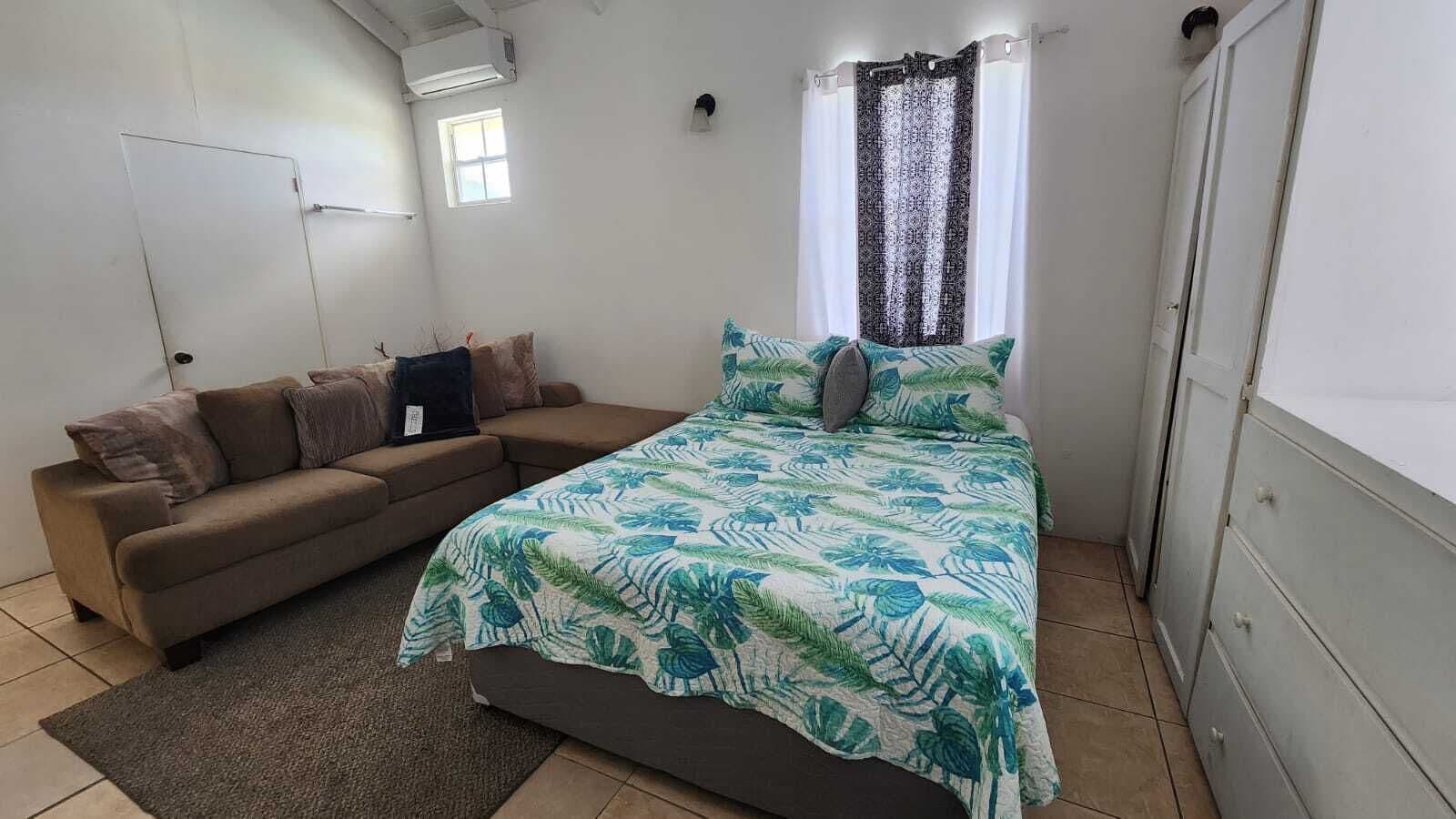 A bedroom with a bed, a sofa, a window with curtains, and a door.