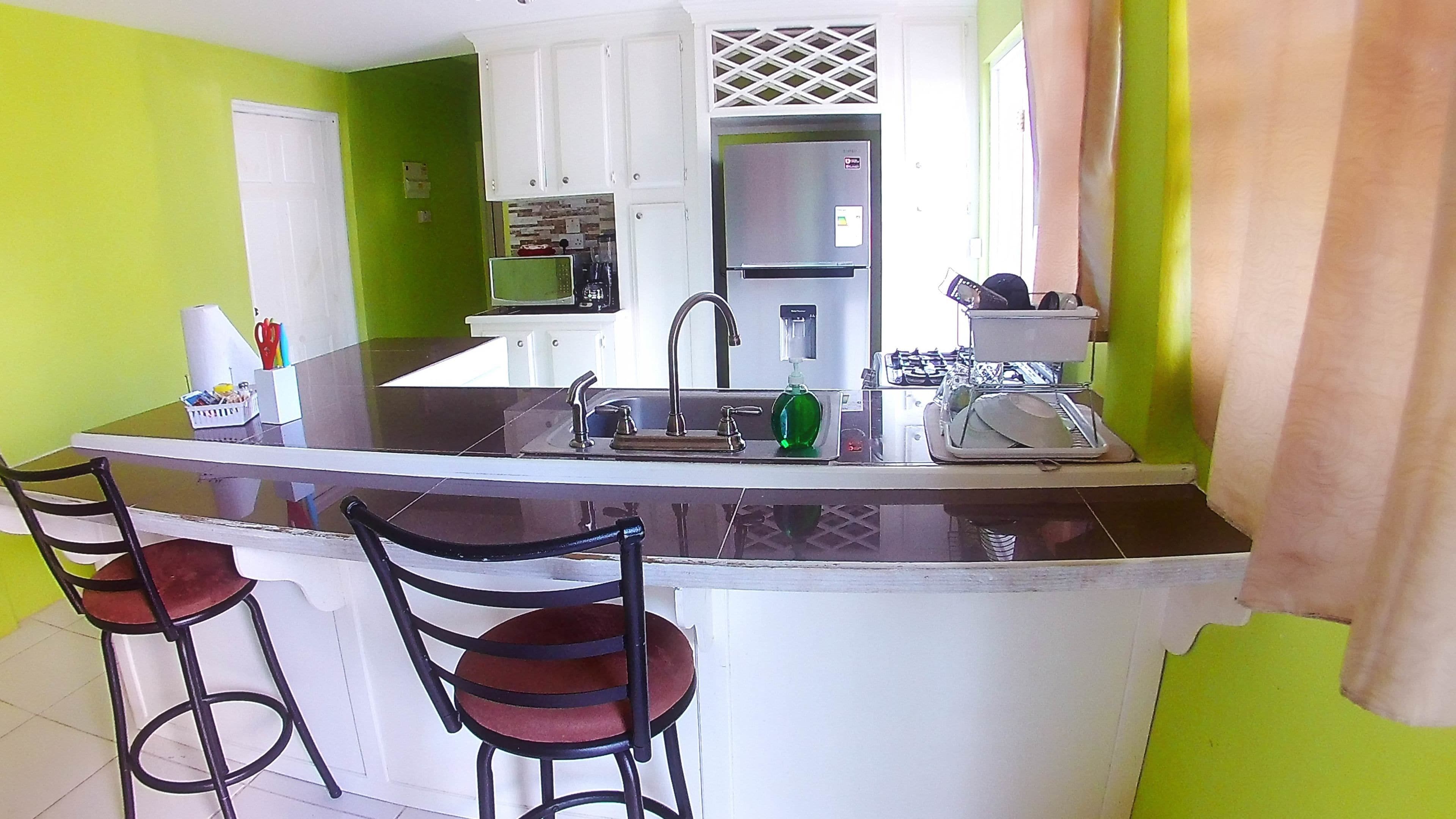 Cocina con una isla central, dos taburetes de bar, un refrigerador de acero inoxidable y un lavamanos con grifo.