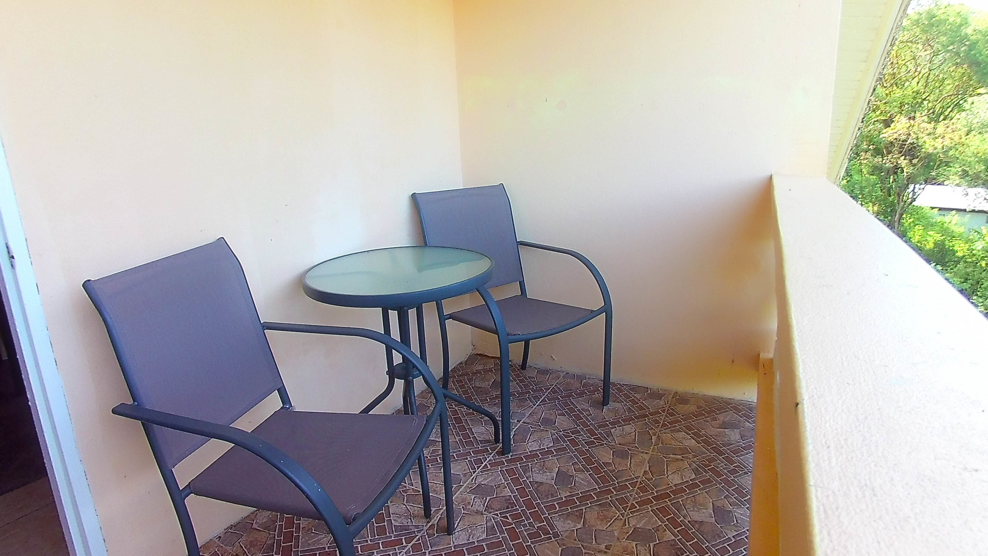 A small balcony with two chairs and a glass table.