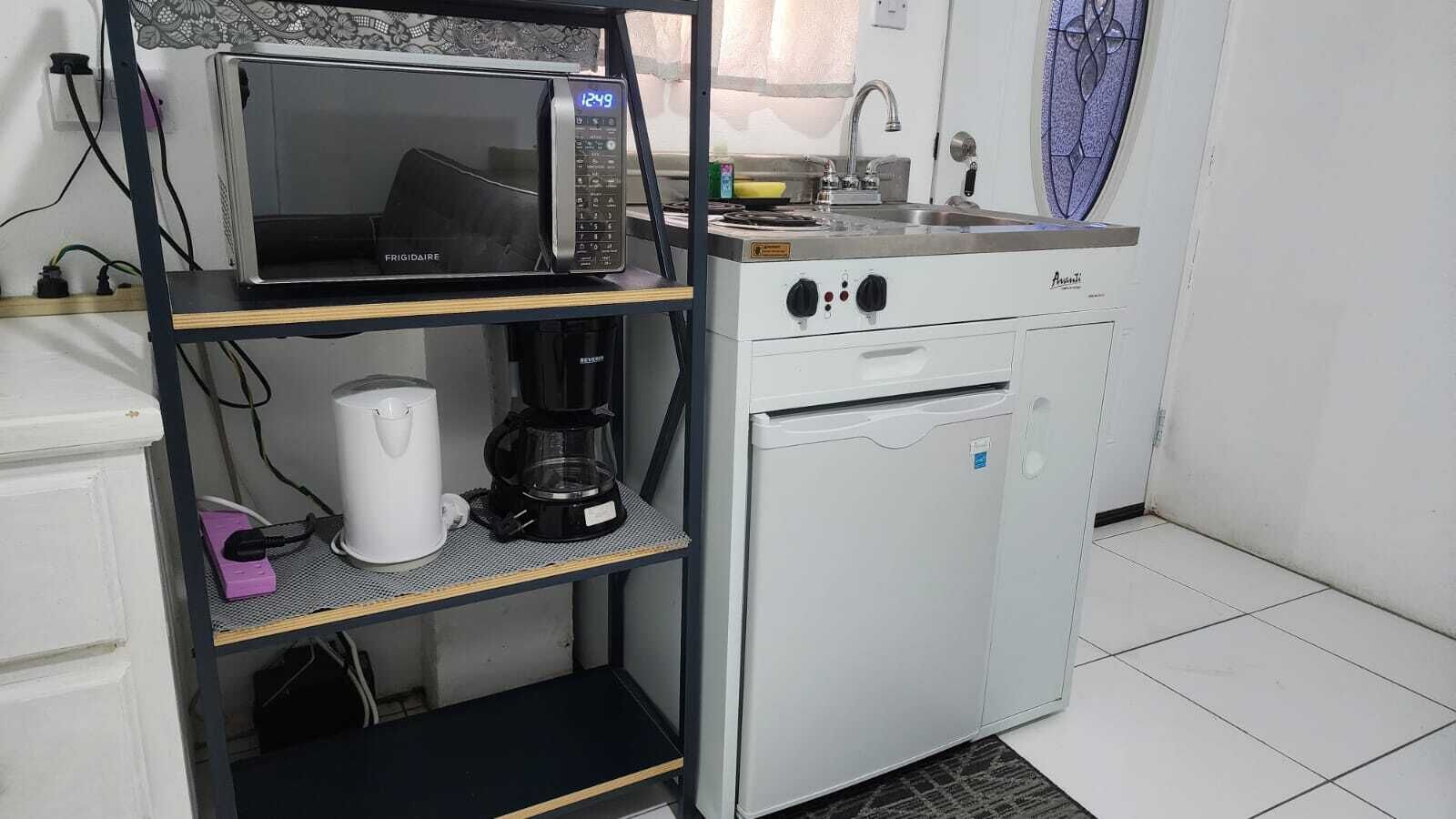 Eine kompakte Küchenzeile mit Mikrowelle, Kaffeemaschine und kleinem Kühlschrank.