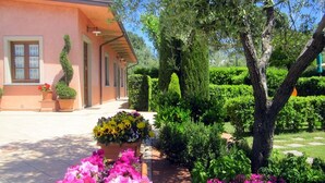 Un jardí ben cuidat amb diverses plantes de flors i setges netament podades davant d'un edifici d'estil arquitectònic clàssic.