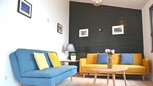A living room with a blue sofa, a yellow sofa, and a round wooden table with a vase of flowers. - CHARMING HOME BETWEEN DOWNTOWN AND THE BEACHES (Noirmoutier-en-l'Île)