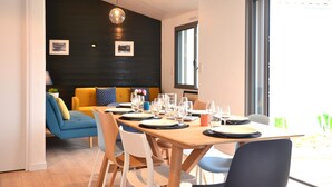A dining area with a wooden table set for four, surrounded by chairs, with a sofa and cushions in the background. - CHARMING HOME BETWEEN DOWNTOWN AND THE BEACHES (Noirmoutier-en-l'Île)