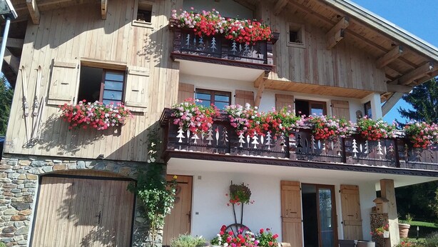 Um chalé de madeira de dois andares com varandas decoradas com floreiras, base de pedra e porta de garagem de madeira.