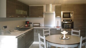 Uma cozinha moderna com ilha central, eletrodomésticos embutidos e área de jantar com mesa redonda e cadeiras.