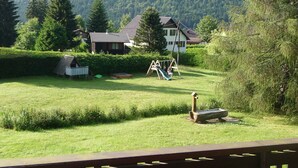 A residential area with a grassy yard, a swing set, and a wooden deck.