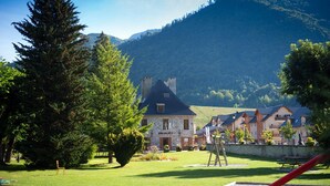 A stone building with a dark roof, surrounded by lush greenery and a mountain backdrop. - ALLEMONT Chalet des Galline DOMAINE VAUJANY ALPE D HUEZ  (Allemond)