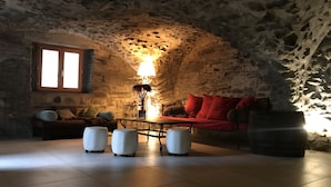 A cozy stone-walled room with a red sofa, a table, and a lamp. - ALLEMONT Chalet des Galline DOMAINE VAUJANY ALPE D HUEZ  (Allemond)