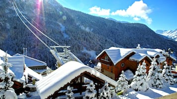Een besneeuwde berglodge met houten hutten en een skilift op de achtergrond.
